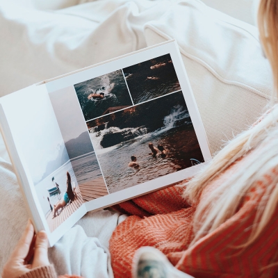 Woman sitting on a sofa looking through a luxury layflat photo book printed by Inkifi, featuring travel photos across seamless pages in natural light