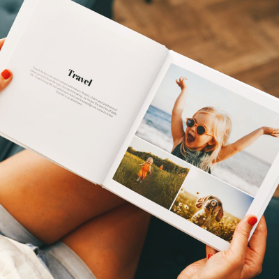 Photo Book With Text open on someone’s lap, showing a Travel chapter title on the left page and a collage of candid child photos on the right page – stylish layflat photo book with personalised text and images, lifestyle scene.